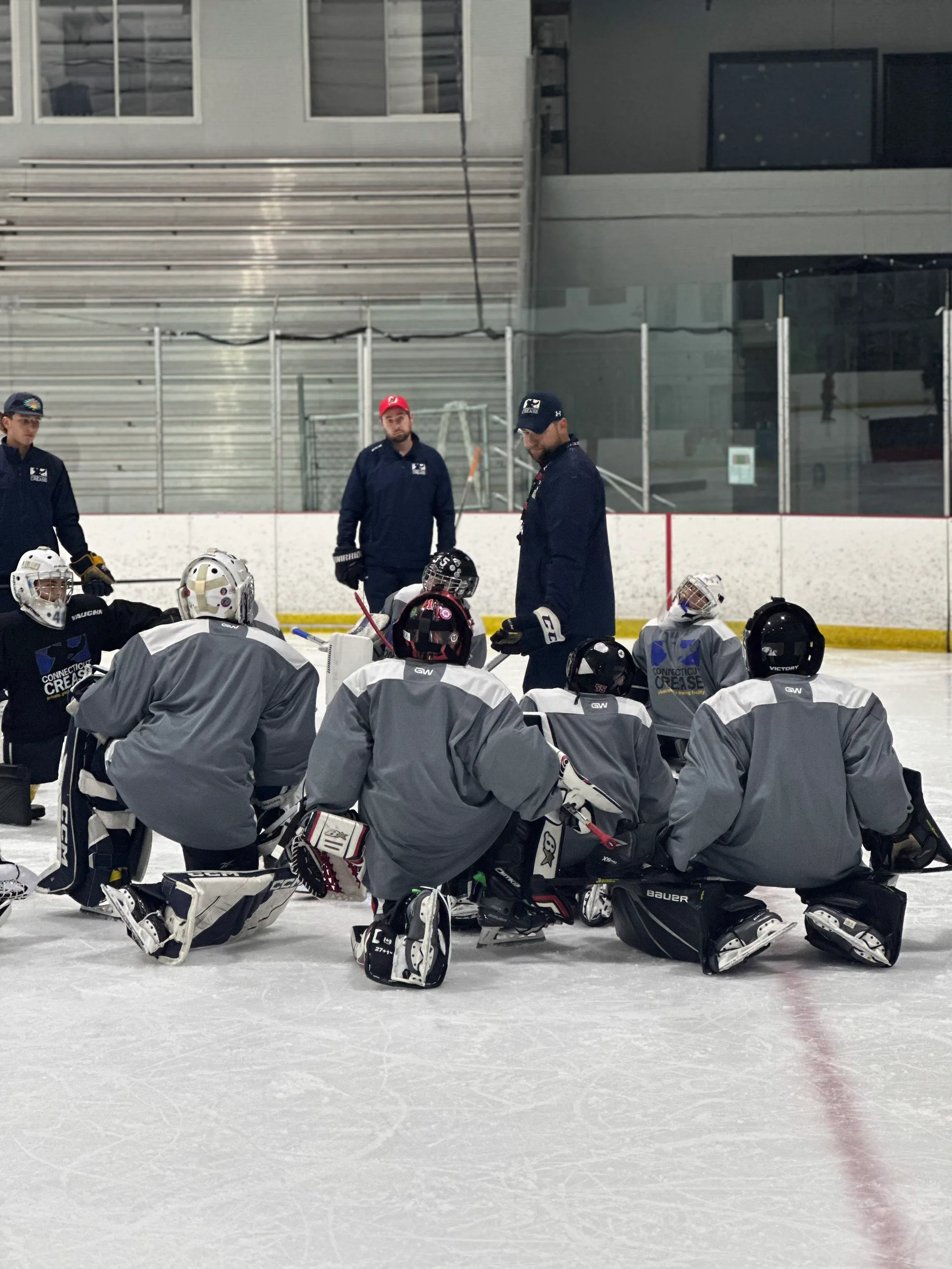 Coaches addressing a group of goalies on the ice